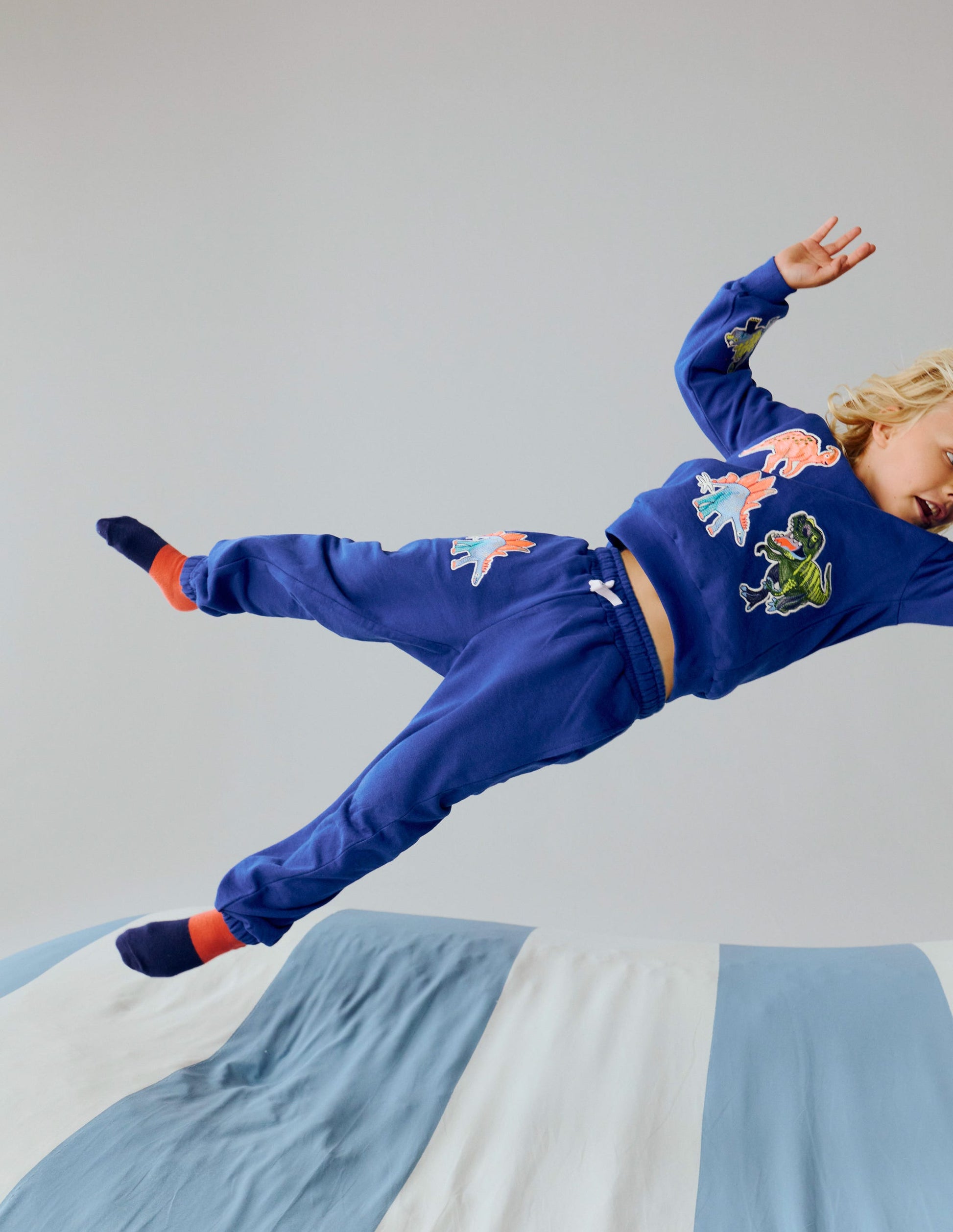 Child in a blue outfit with colorful designs jumping on a bed.
