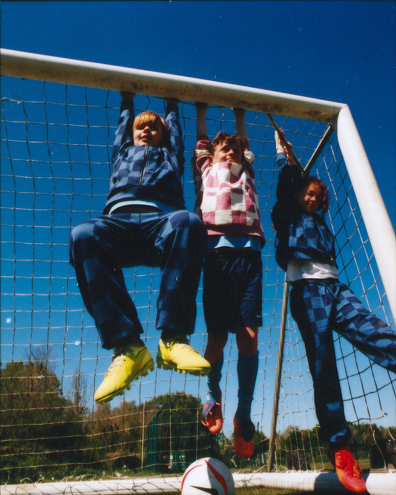 Three children playing on a soccer goal网, with a clear blue sky in the background.
