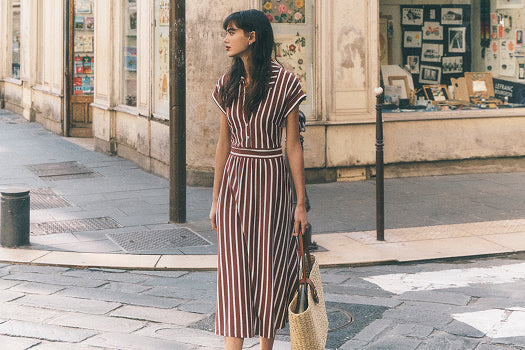Woman in a striped dress standing on a street with a store in the background