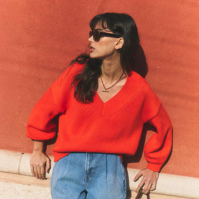 Woman wearing a red sweater and blue jeans against a red wall.