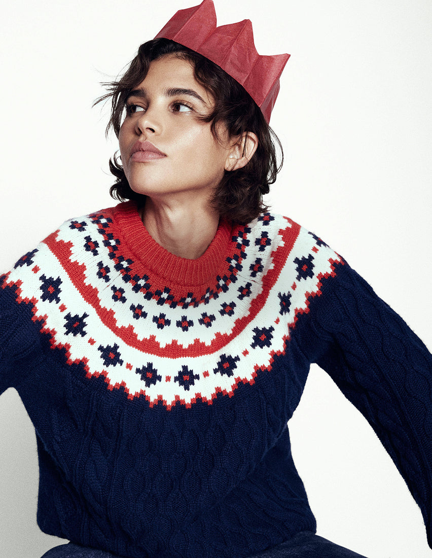 Person wearing a festive sweater with a red paper crown on a white background