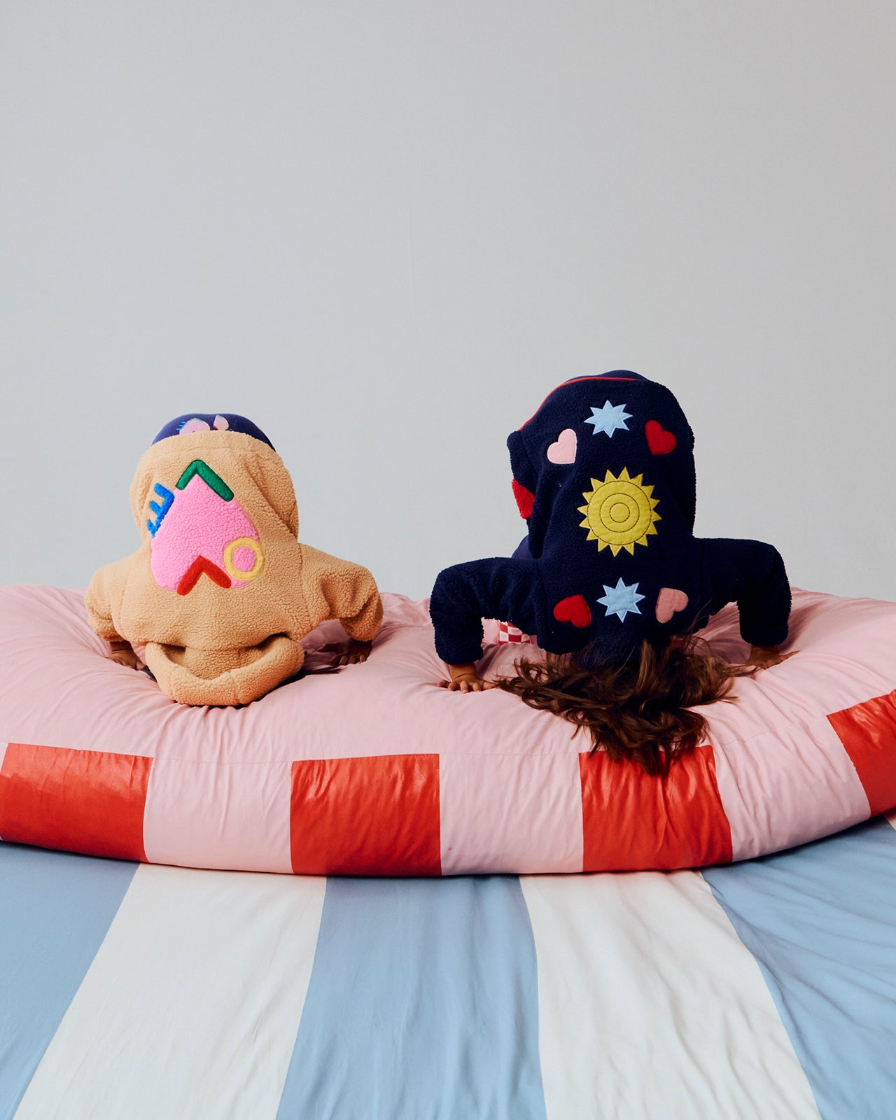 Two children wearing colorful animal-themed hoodies sitting on a striped bed.