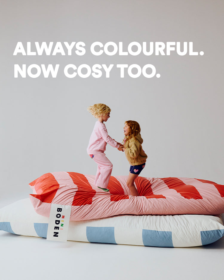 Two children playing on a colorful bed with 'Boden' branding, text 'Always Colourful. Now Cosy Too.' above.