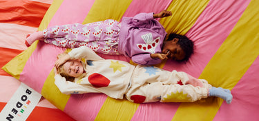 Two children in colorful pajamas lying on a striped pink and yellow blanket with a Boden sign.