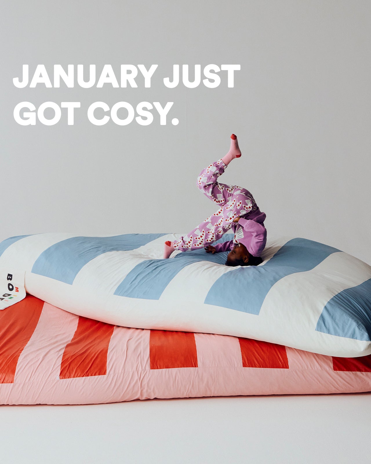 Person in pajamas standing on a colorful comforter with text 'January just got cosy' on a plain background