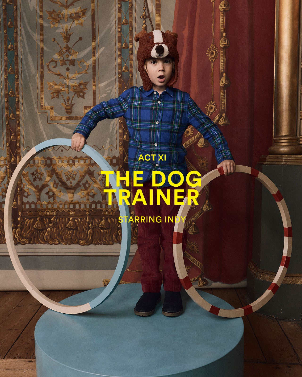 Child in bear costume with hoops, posing theatrically against a decorative wall.