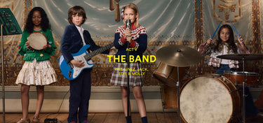 Four children playing musical instruments with a decorative wall in the background