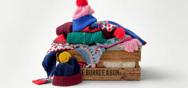 Stack of colorful knit hats on a wooden crate with 'Burree & Son' branding.