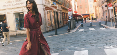 Woman in a red dress walking on a city street with buildings and signs in the background.