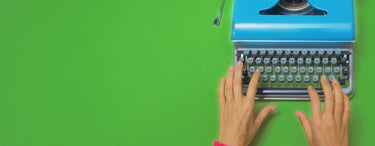 Blue typewriter on a green background with hands typing.