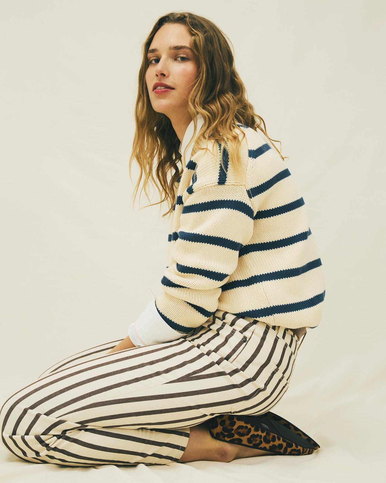 Woman wearing a striped sweater and pants sitting on the floor against a plain background