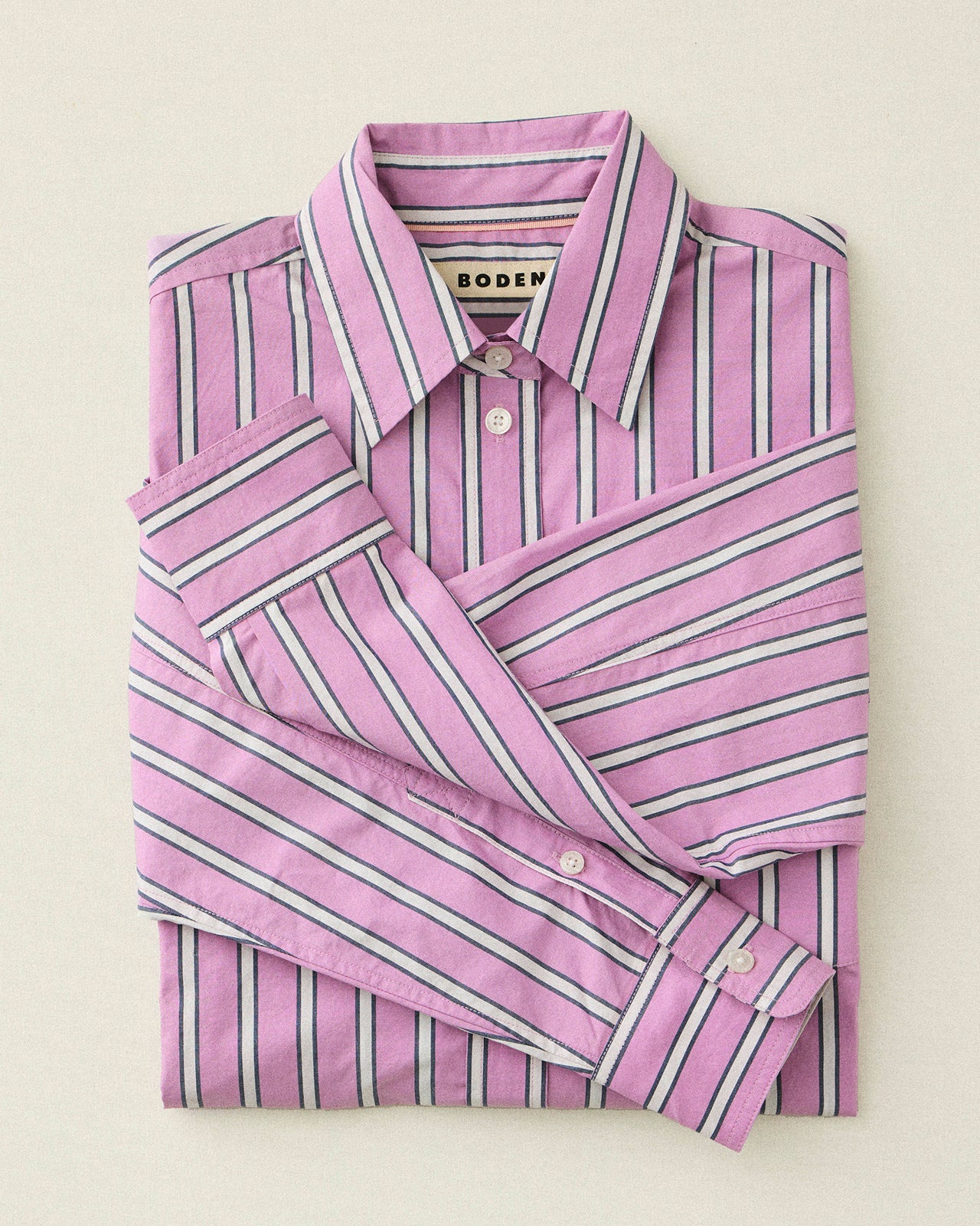 Folded pink and white striped shirt with 'Boden' branding on a light beige background