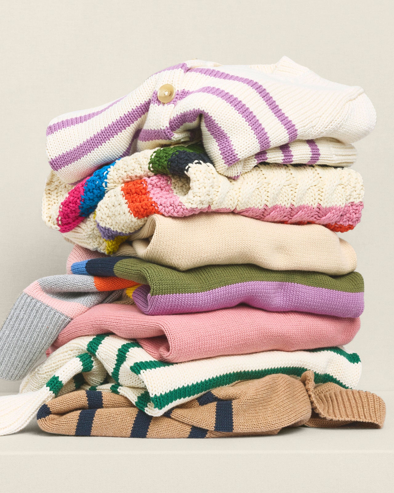 Stack of colorful knitted sweaters on a light background