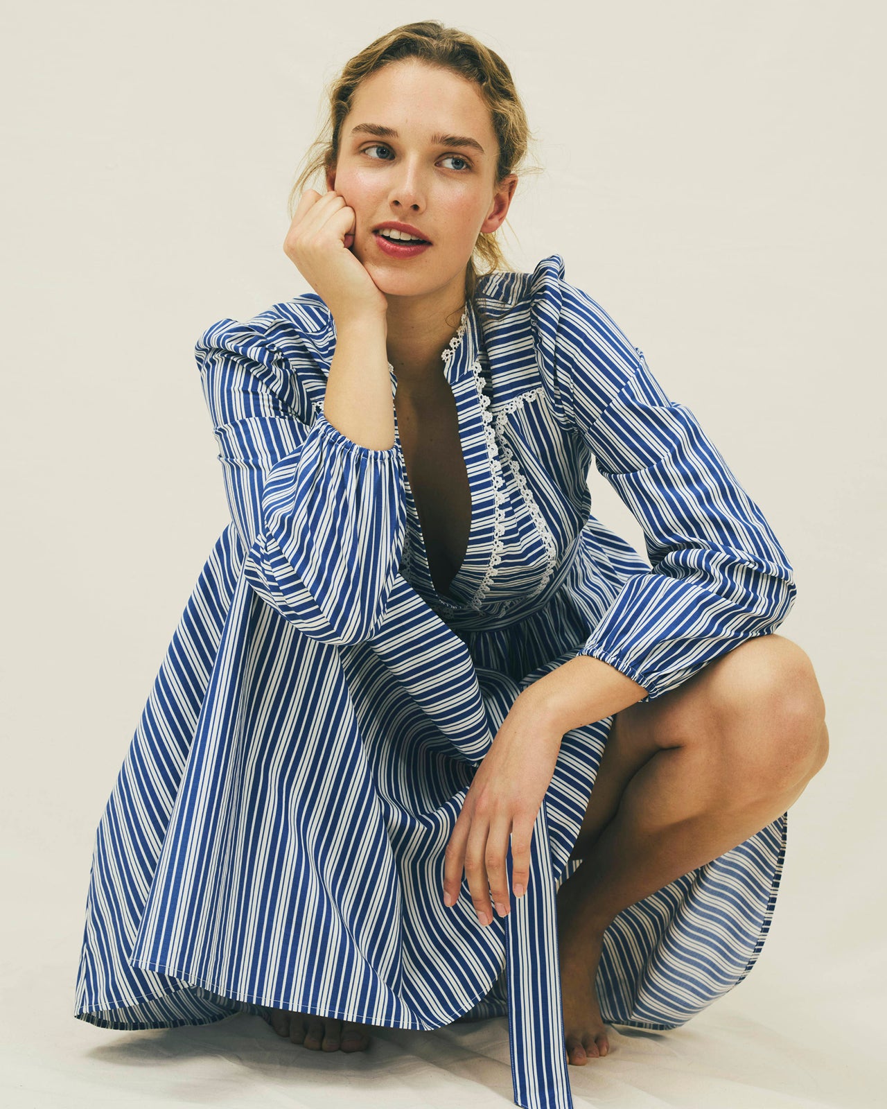 Woman wearing a blue and white striped dress sitting on a light-colored floor.
