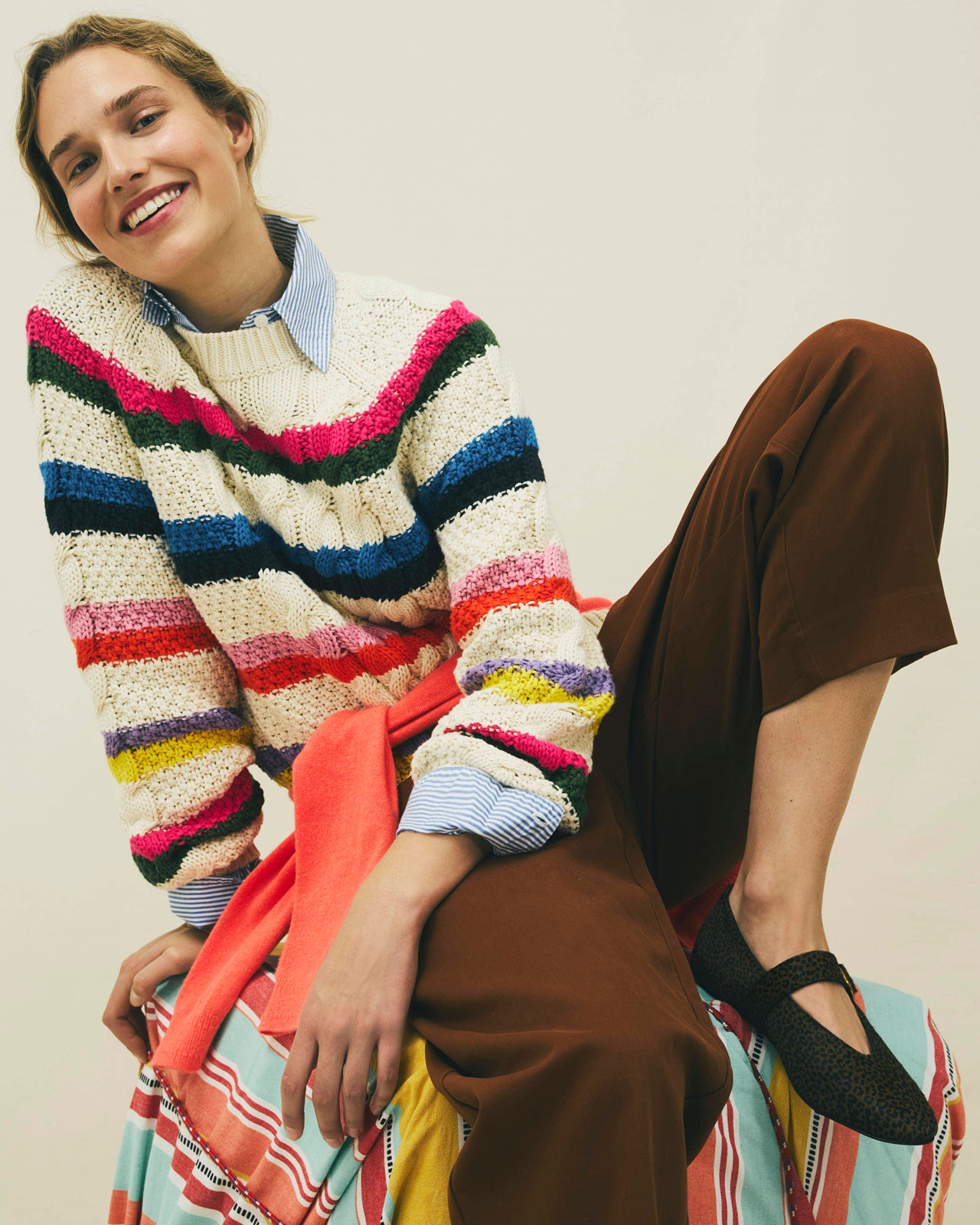 Person wearing a colorful striped sweater and brown pants sitting on a chair.