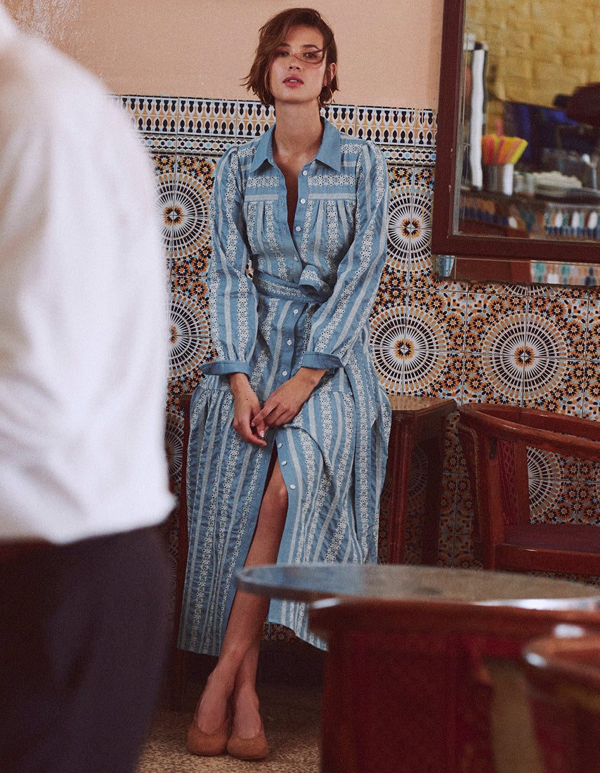 Woman in a blue patterned dress standing in a room with decorative tiles.