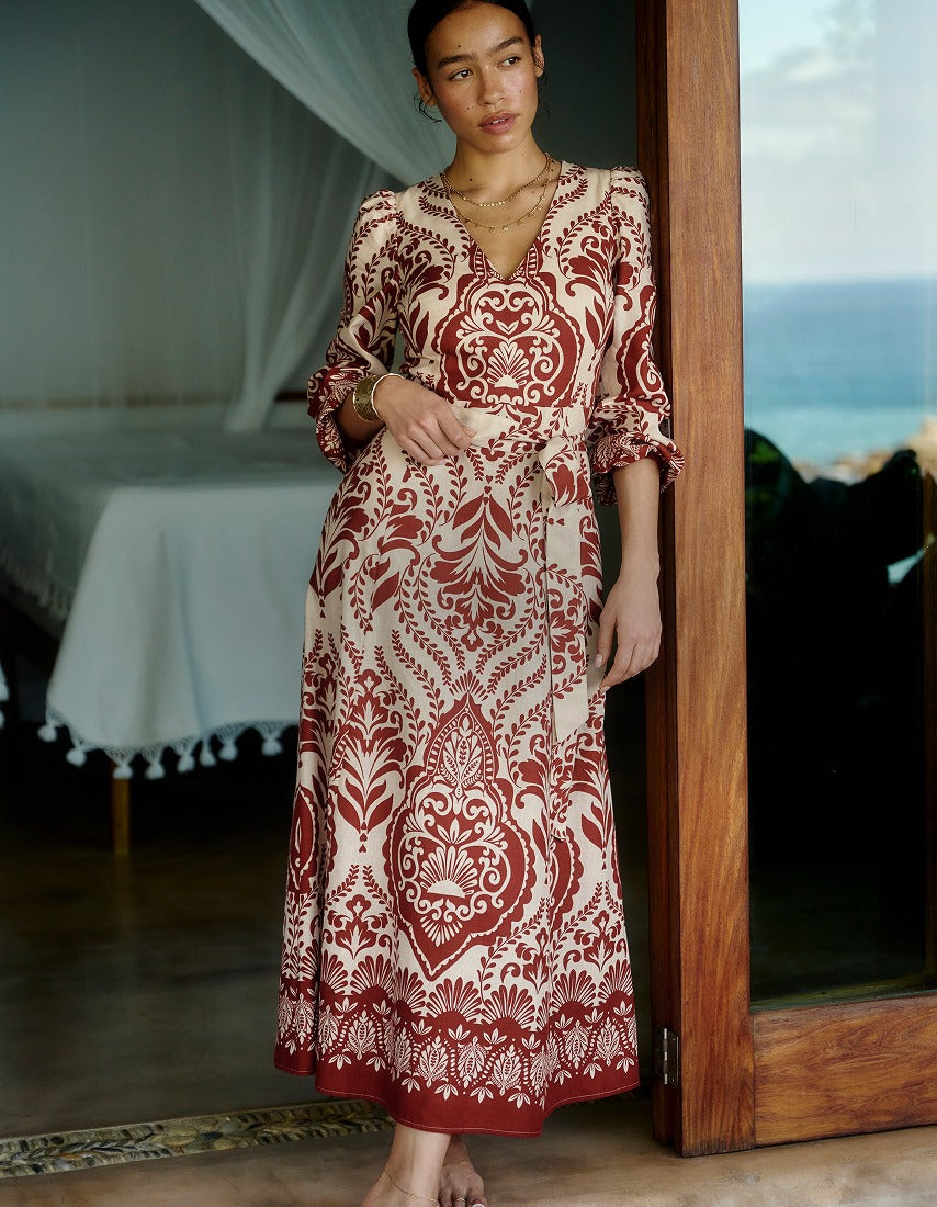 Woman wearing a patterned dress standing in a room with a bed and window.