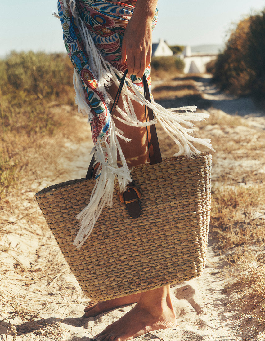 Person holding a woven bag with fringes on a sandy path