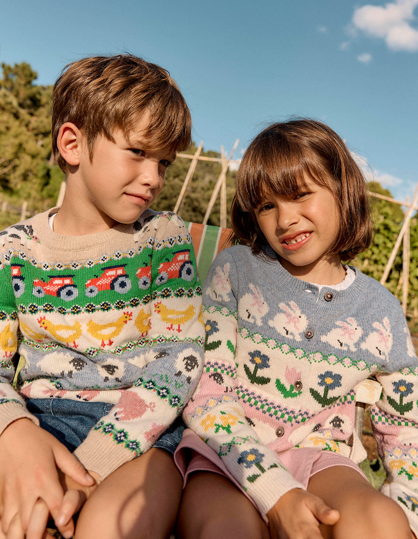 Two children wearing patterned sweaters sitting outdoors with a clear blue sky.