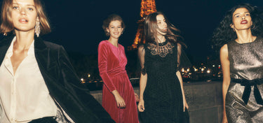 Four women in formal attire standing in front of the Eiffel Tower at night.