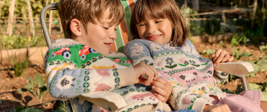 Two children sitting on a chair outdoors, wearing patterned sweaters.