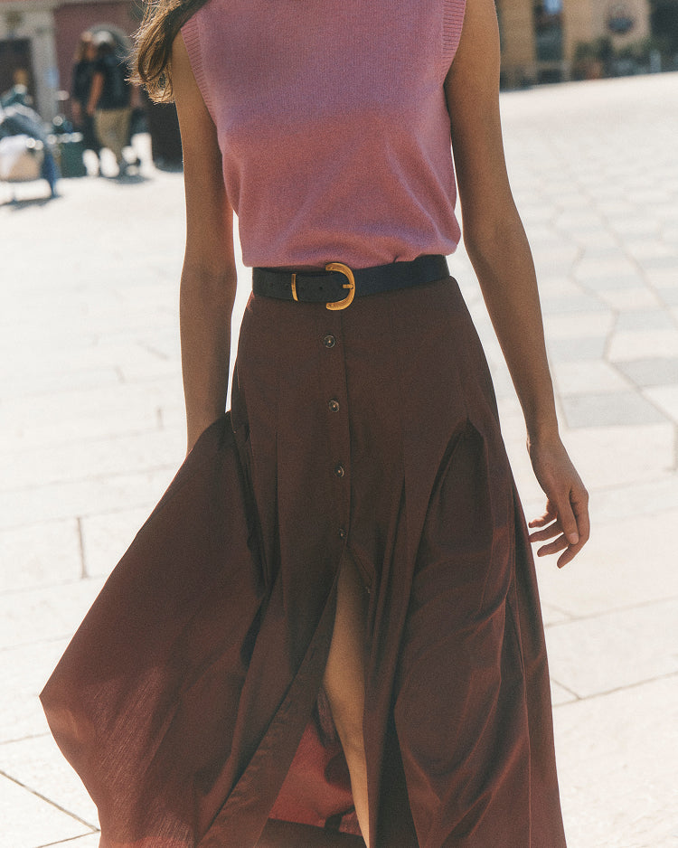 Person wearing a pink sleeveless top and brown skirt with a blurred background