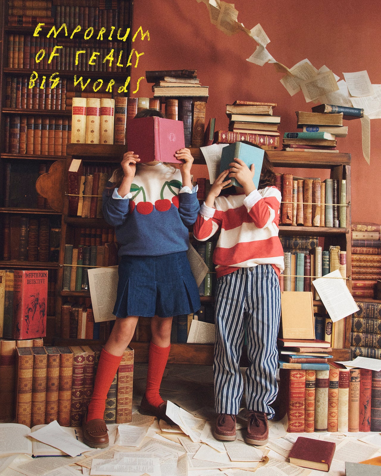 Two children in a room filled with books, holding books over their faces.