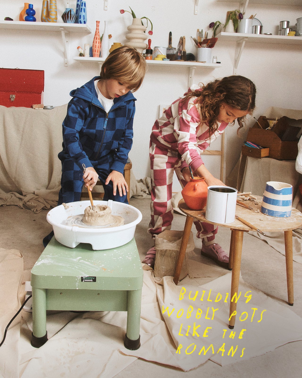 Two children working with a potter's wheel in a home setting.