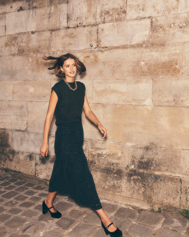 Woman in a black dress standing against a stone wall.