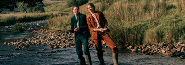 Two people standing by a river with a scenic background