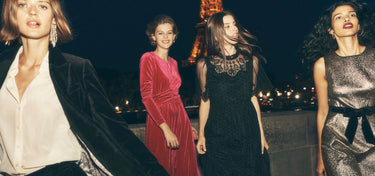Four women in formal attire standing in front of the Eiffel Tower at night.