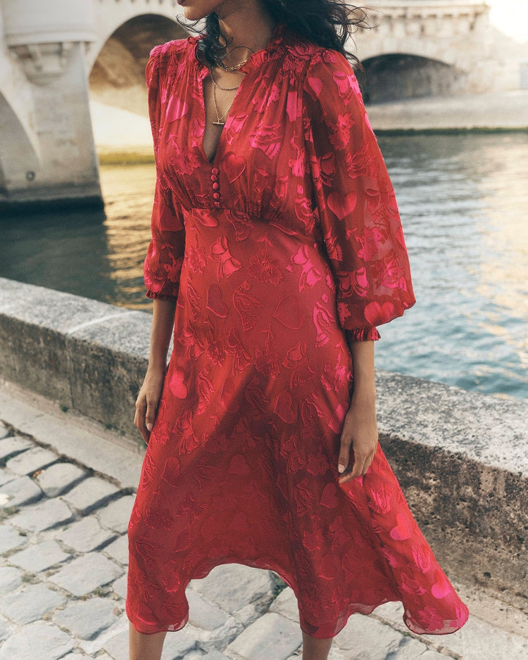 Woman in a red dress standing by a river with a bridge in the background