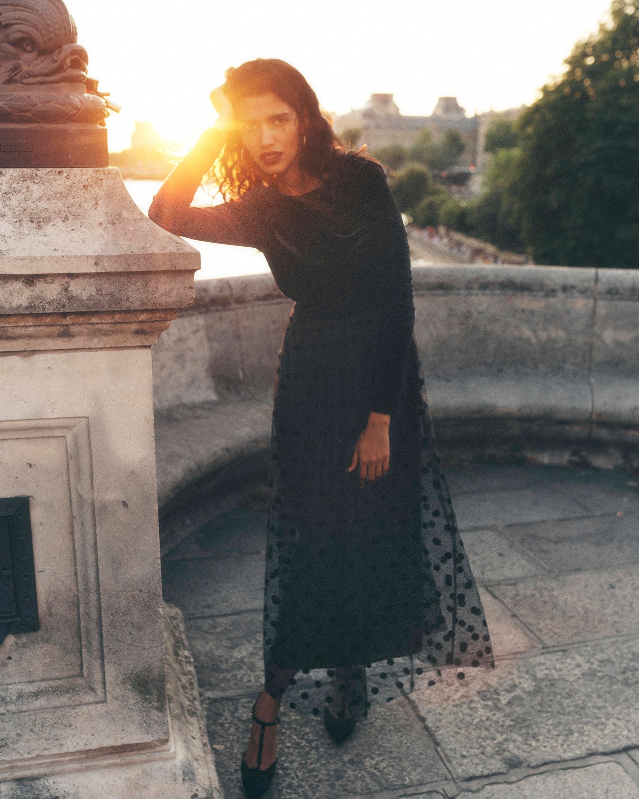 Woman in a black dress standing on a stone ledge with sunset light